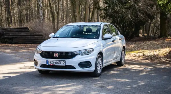 Biały Fiat Tipo sedan zaparkowany na leśnej drodze.