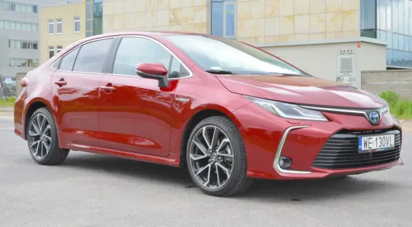 Czerwona Toyota Corolla 1.8 Hybrid z nowoczesnymi felgami stoi przed budynkiem.