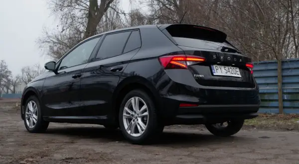 Czarna Skoda Fabia 2024 z polskimi tablicami rejestracyjnymi stoi na brudnej drodze, otoczona drzewami.
