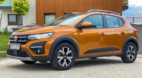 Pomarańczowy Dacia Sandero Stepway na tle nowoczesnego budynku. Sprawdź atrakcyjne dacia sandero - ceny.