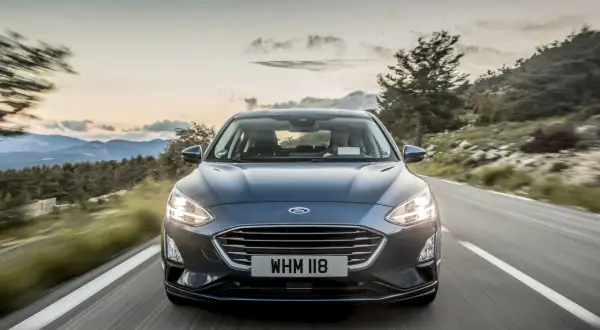 Ciemny Ford Focus MK5 jedzie krętą drogą wśród gór. Słońce zachodzi, tworząc piękne niebo.