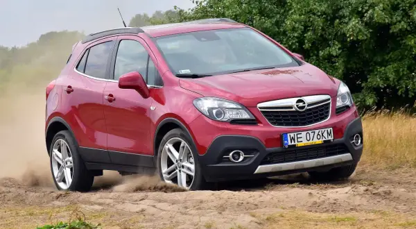 Czerwony Opel Mokka 2015 na piaszczystej drodze, unoszący kurz.