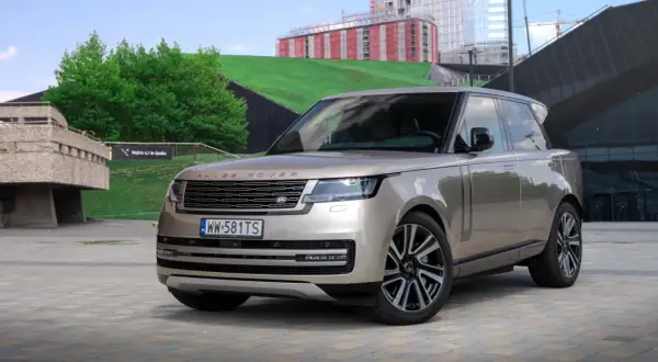 Elegancki Range Rover 2025 w kolorze piaskowym prezentuje się na tle nowoczesnej architektury.