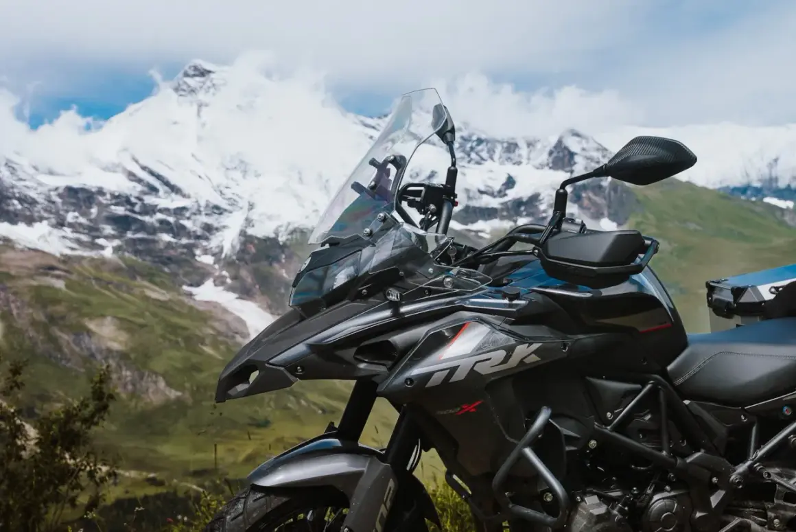 Ciemny motocykl turystyczny na tle ośnieżonych gór i zielonej doliny.