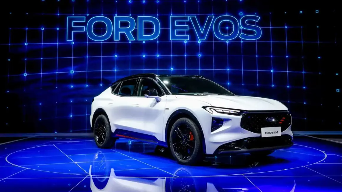 Biały Ford Evos na niebieskiej scenie z napisem "FORD EVOS" w tle.