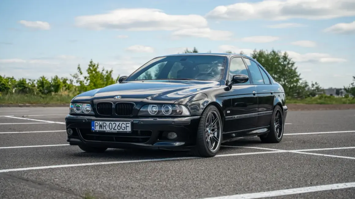 Czarne BMW E39 na parkingu, z widocznym przodem i bokiem samochodu.