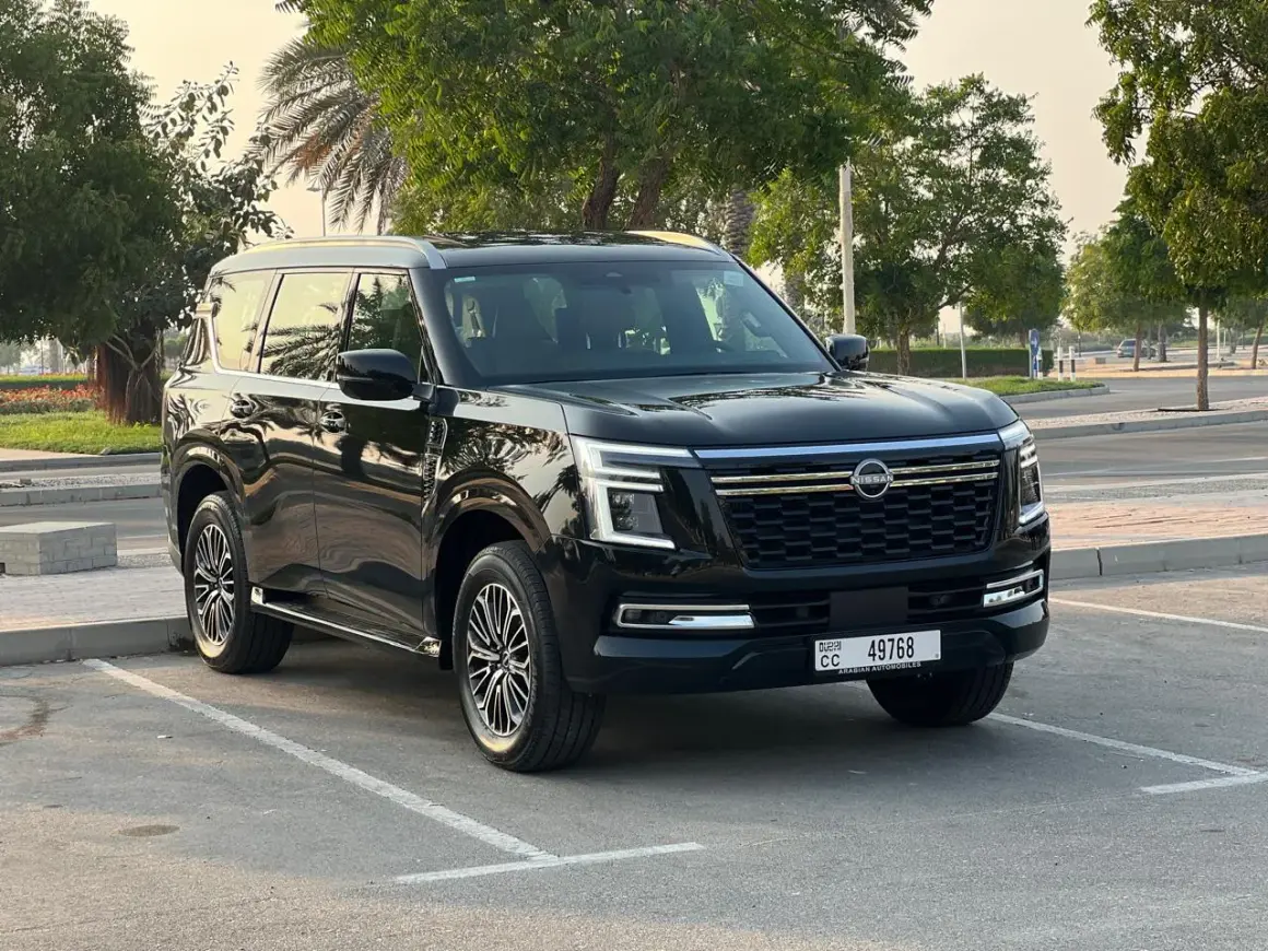 Czarny Nissan Patrol 2025 zaparkowany na tle drzew i palmy.