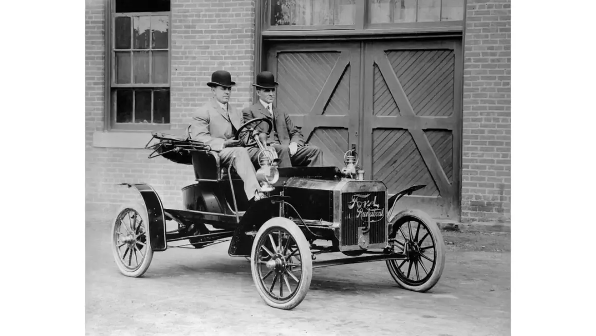 Dwóch dżentelmenów w melonikach siedzi w zabytkowym Fordzie Model T Runabout, gotowych na przejażdżkę.