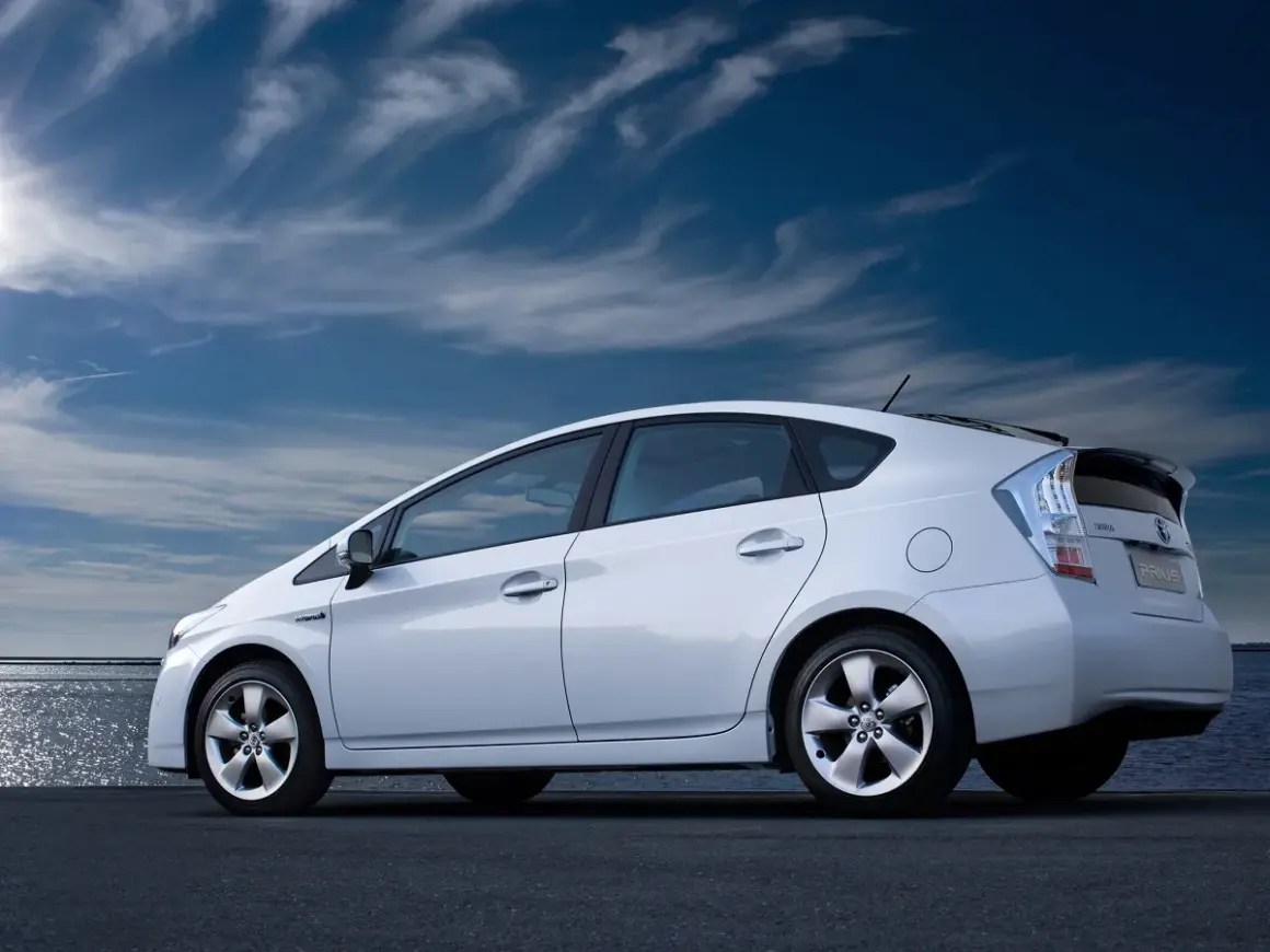 Biały Toyota Prius 3 na tle błękitnego nieba z chmurami.