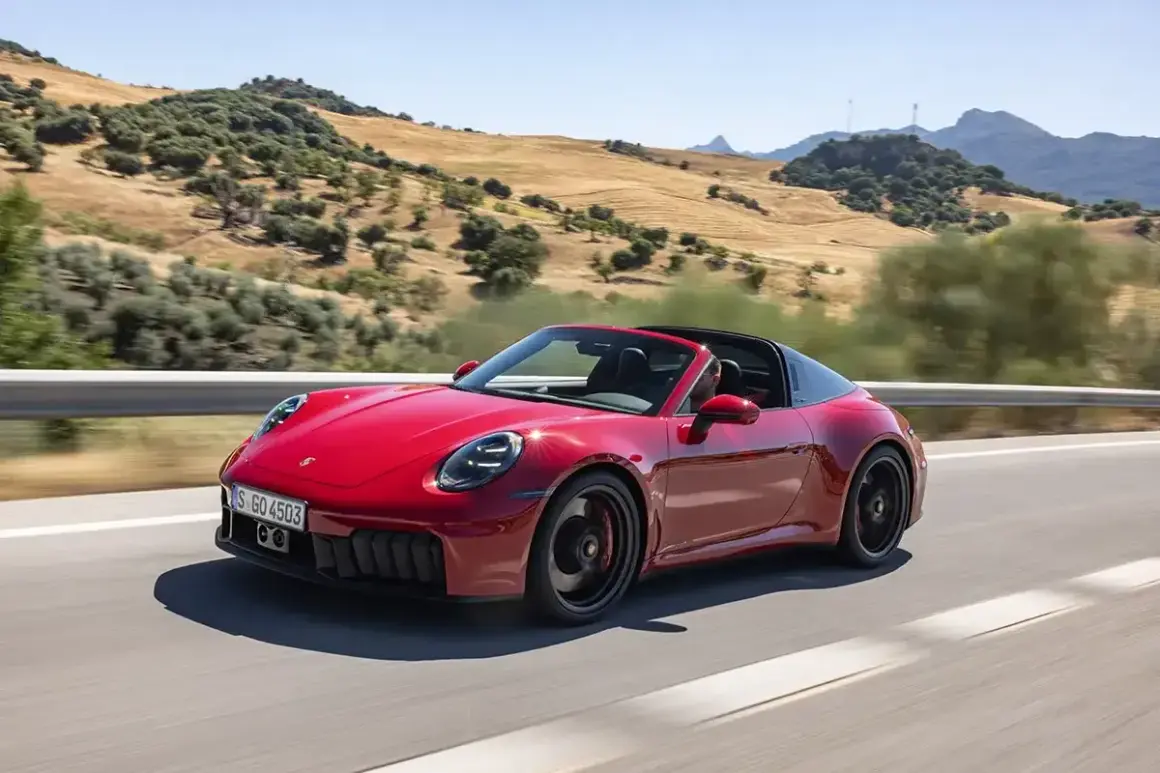 Czerwony Porsche 911 Carrera 4 GTS Targa sunie po krętej drodze wśród wzgórz.