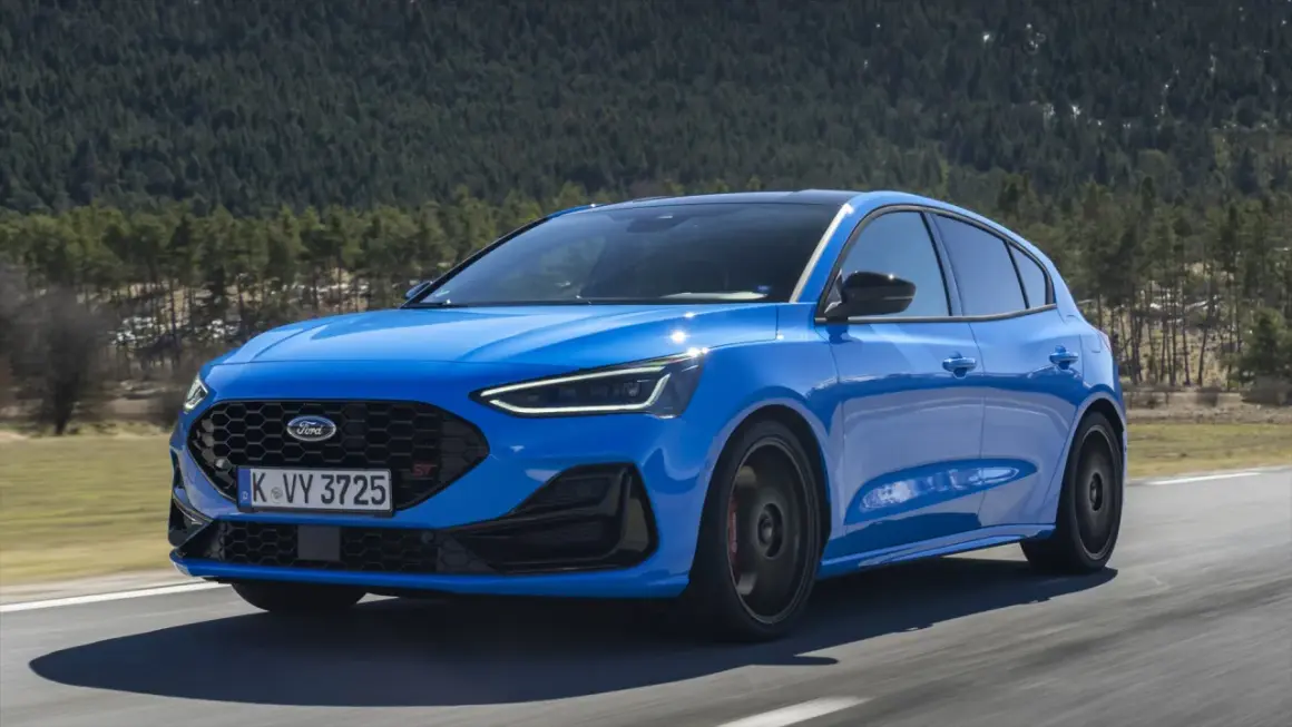 Niebieski Ford Focus ST na drodze, zalesione wzgórza w tle.