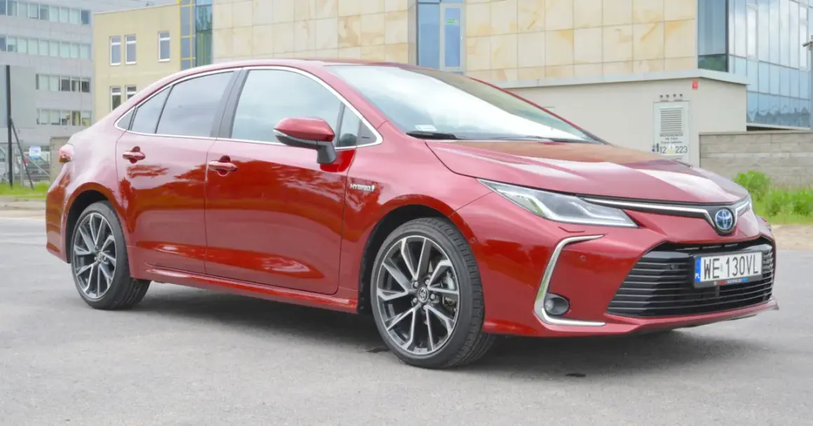 Czerwona Toyota Corolla 1.8 Hybrid z nowoczesnymi felgami stoi przed budynkiem.