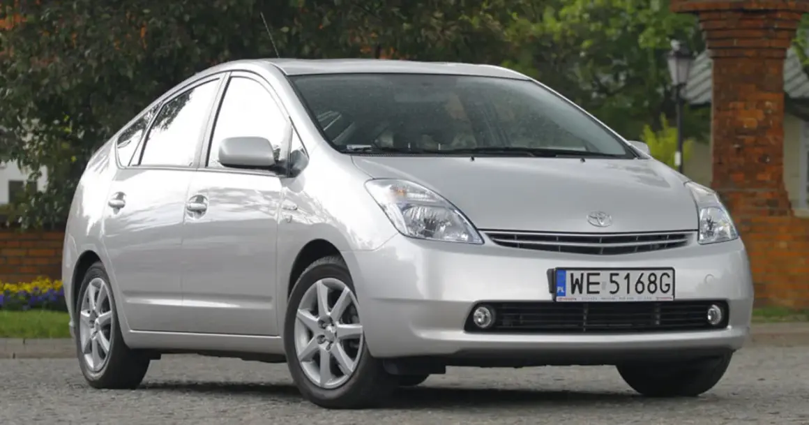 Srebrny Toyota Prius 2 zaparkowany przed ceglanym budynkiem.