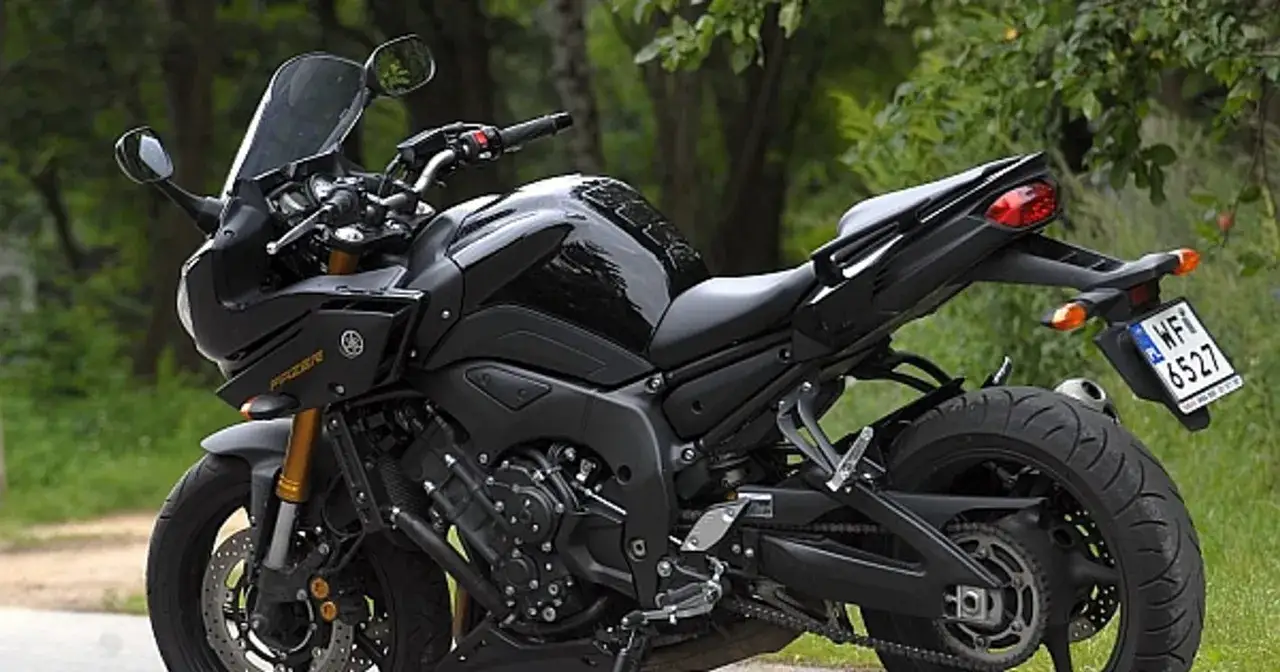 Czarny motocykl Yamaha FZ z przyciemnianą szybą, gotowy do jazdy po leśnej drodze.