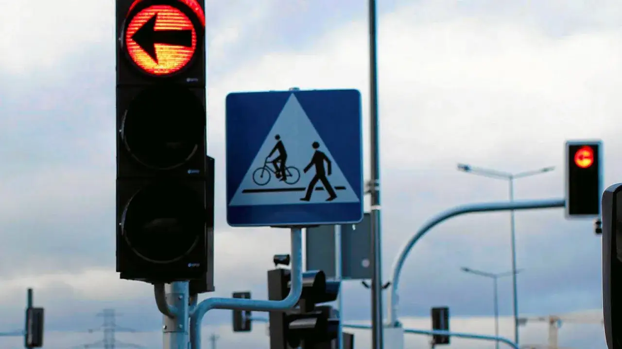 Sygnalizator S3 świeci na czerwono ze strzałką w lewo. Obok znak drogowców z rowerzystą i pieszym.