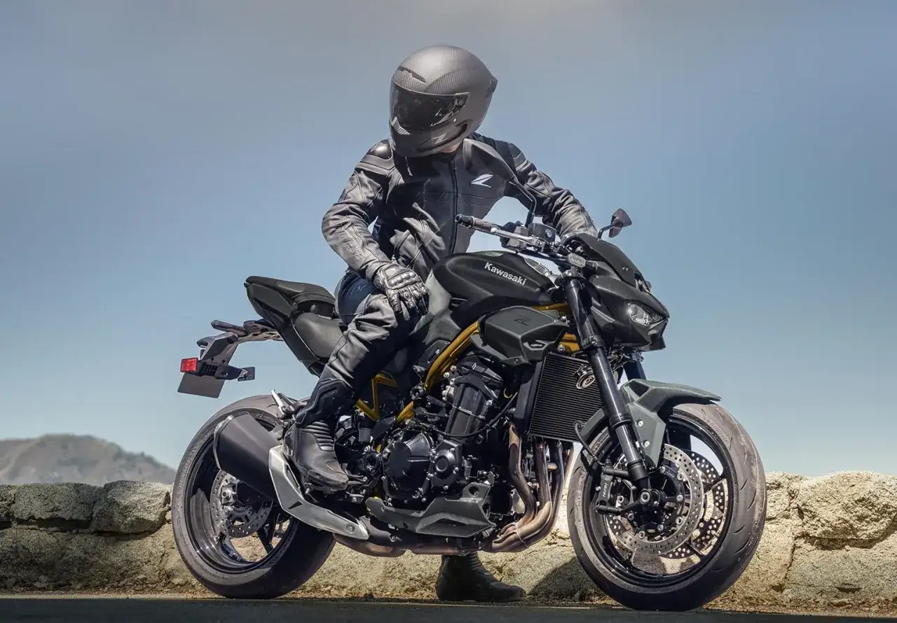 Motocyklista w czarnej skórze siedzi na czarnym Kawasaki Z900 z żółtą ramą, gotowy do jazdy.