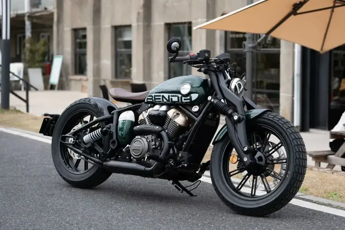 Stylowy, zielony chopper motor z brązowym siedzeniem i czarnymi felgami, zaparkowany na ulicy.