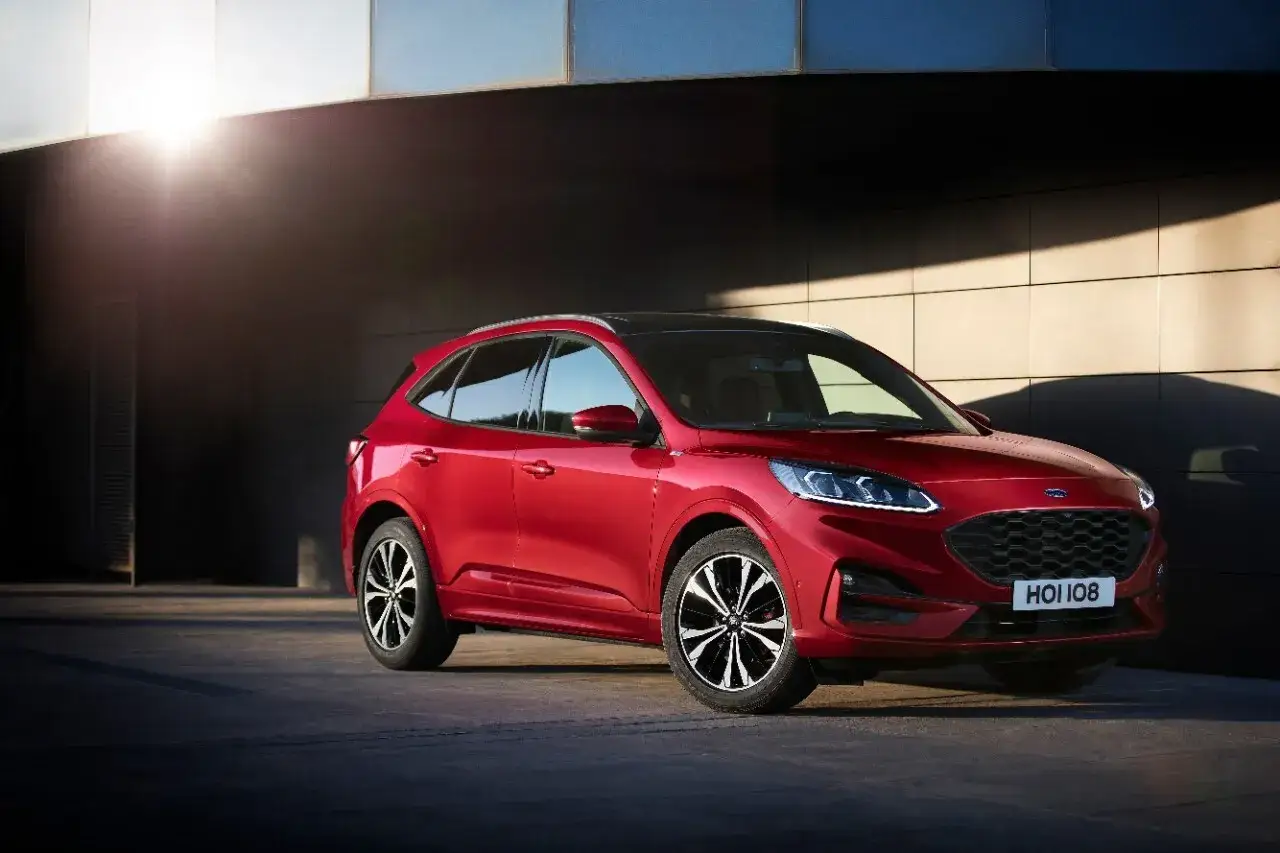 Czerwony Ford Kuga prezentuje swoje dynamiczne linie i imponujące ford kuga wymiary. Stylowy SUV na tle nowoczesnej architektury.