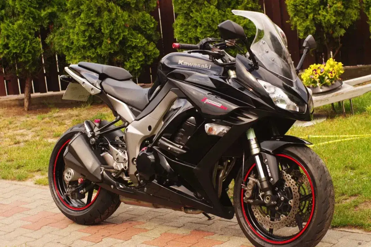 Czarny motocykl Kawasaki Z 1000 z czerwonymi akcentami na felgach, zaparkowany na podjeździe z zielenią w tle.
