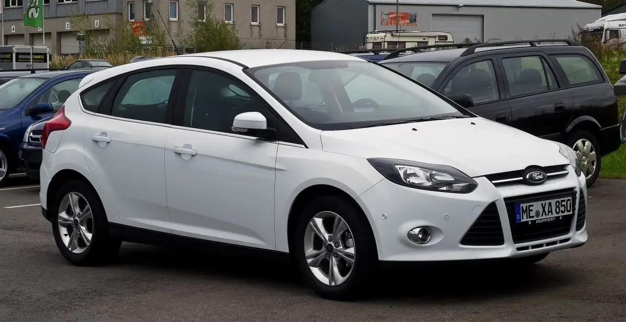 Biały Ford Focus MK3 1.6 benzyna, zaparkowany obok czarnego kombi.