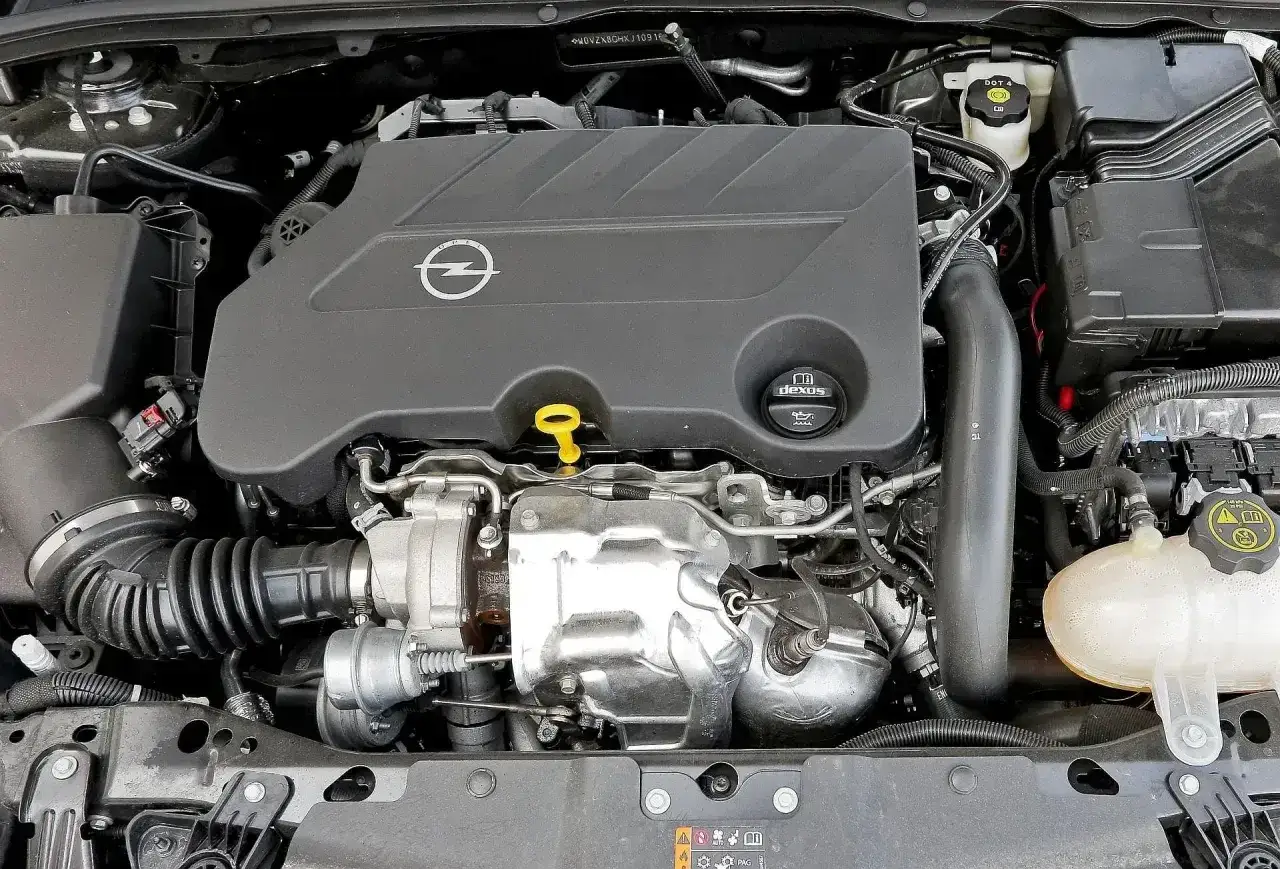 Silnik 2.0 turbo w Oplu Insignia, widok z góry. Widać turbosprężarkę, osłonę silnika z logo Opla i korek oleju.