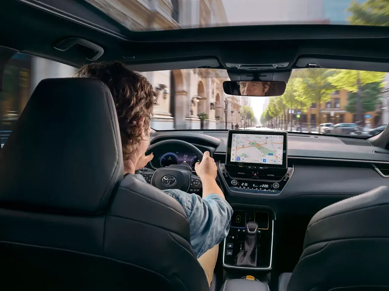 Wnętrze nowego Corolla Cross 2025 z kierowcą korzystającym z nawigacji na dużym ekranie.