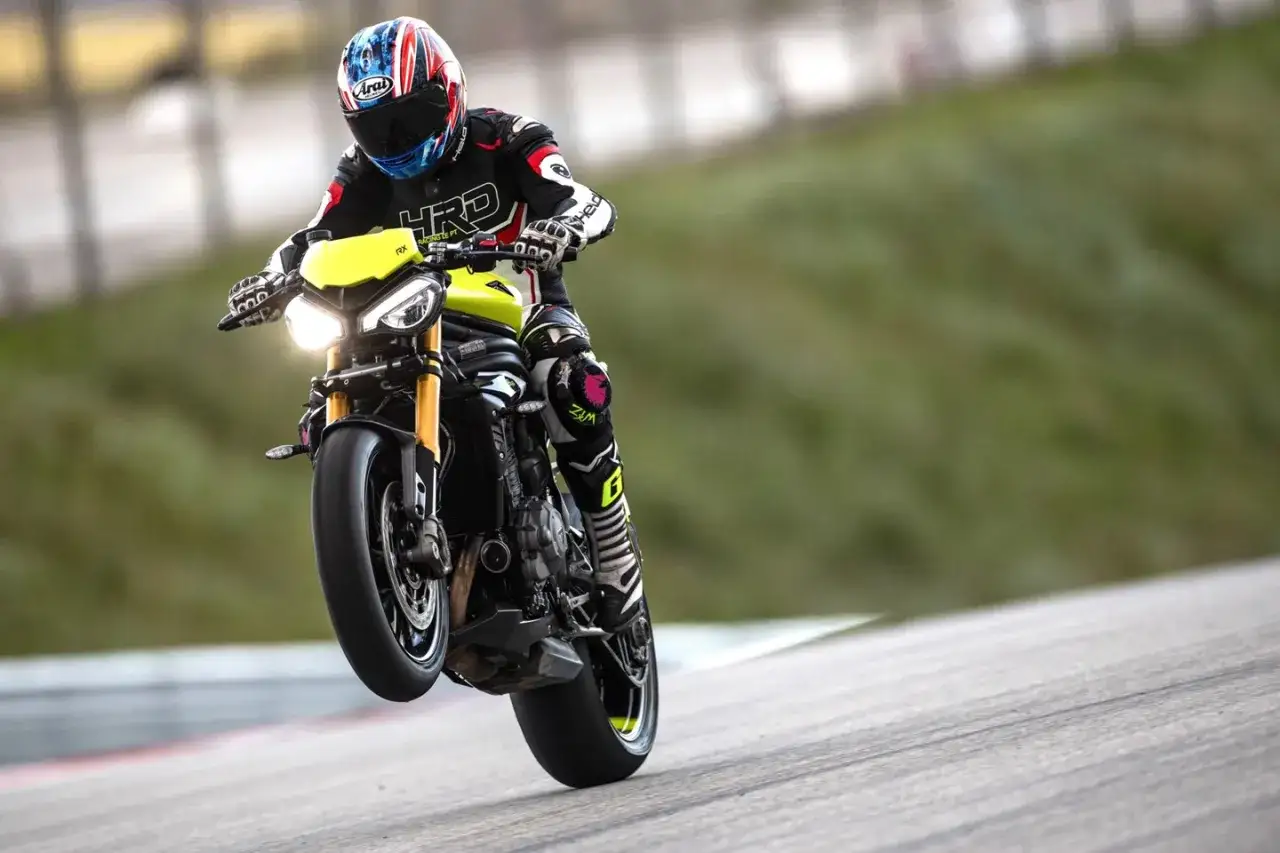 Motocyklista na torze wykonuje wheelie na motocyklu Triumph Speed Triple.