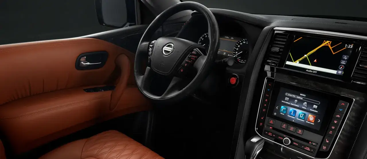 Wnętrze luksusowego Nissan Patrol 2025 z brązową skórzaną tapicerką, multimedialnym ekranem nawigacji i przyciskiem start/stop.