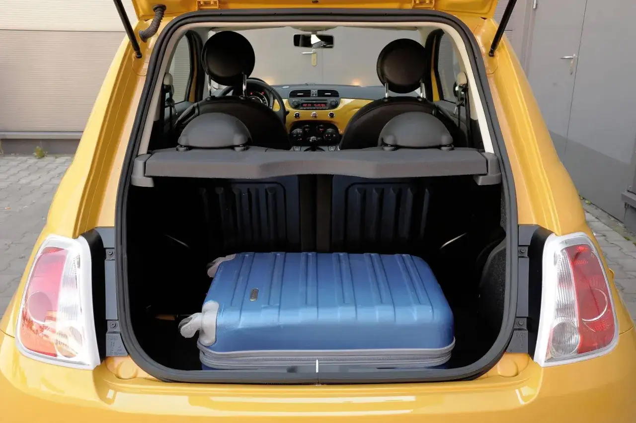 Żółty Fiat 500 XL z otwartym bagażnikiem, w którym znajduje się duża, niebieska walizka.