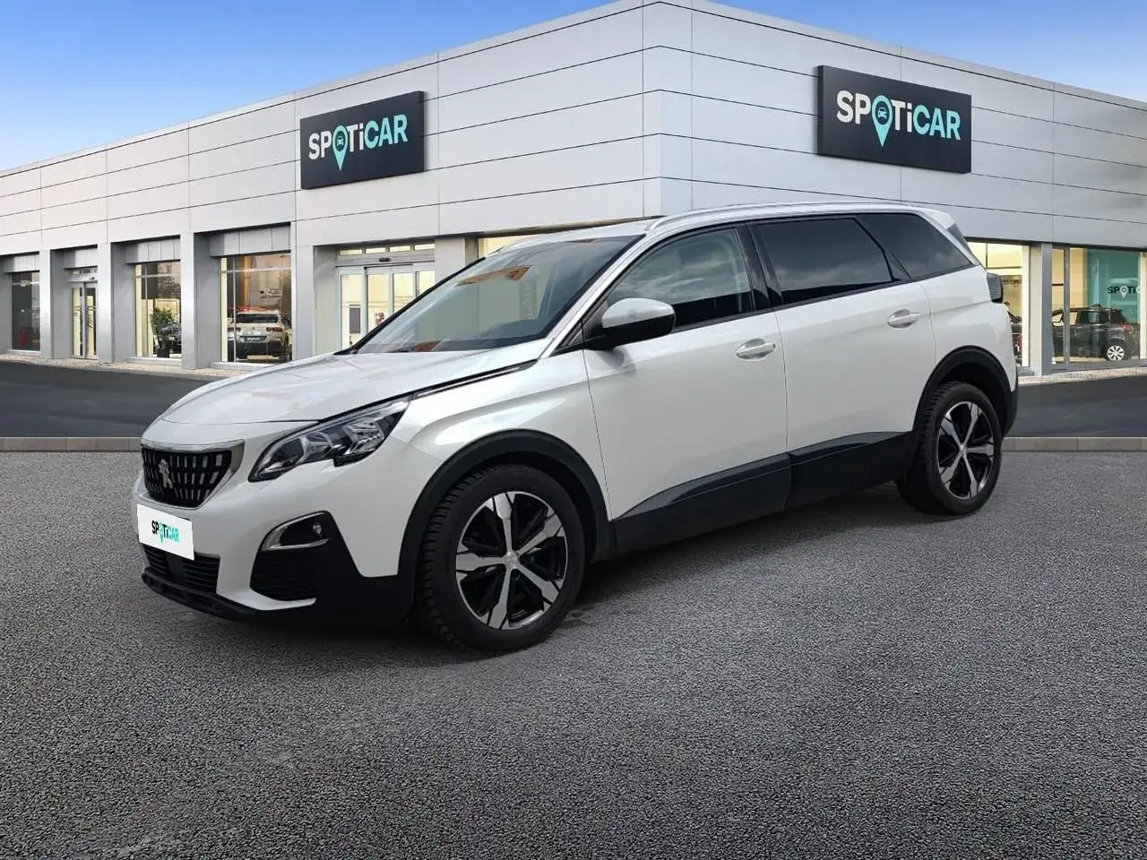 Biały Peugeot 5008 2.0 HDI zaparkowany przed salonem Spoticar. Elegancki SUV z czarnymi dodatkami.