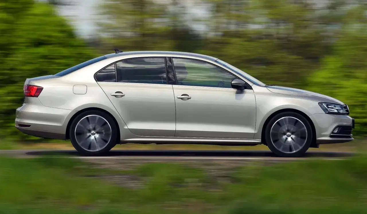 Srebrny VW Jetta MK6 w ruchu, z rozmytym tłem zieleni i drogi.