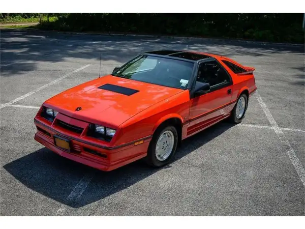 Pomarańczowy Dodge Daytona z czarnym dachem i spojlerem na parkingu.