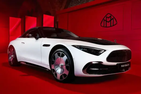 Elegancki biały Maybach z czarnym dachem na czerwonym tle. Logo Maybach widoczne na ścianie. Poznaj jego wyjątkową maybach cena.