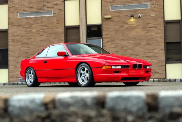 Czerwone BMW serii 8 (E50) z lat 90. zaparkowane przed budynkiem z cegły.