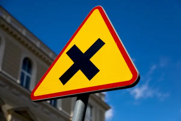 Żółty trójkąt z czarnym znakiem "X" ostrzega o skrzyżowaniu dróg. Uważaj, bo to droga z pierwszeństwem.