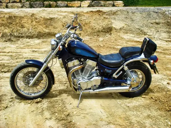Błękitny motocykl Suzuki Intruder z chromowanymi elementami i czarnym siedzeniem stoi na piaszczystym podłożu.