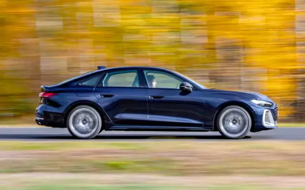 Ciemnoniebieskie Audi A4 B10 w ruchu, z rozmytym tłem jesiennych drzew.