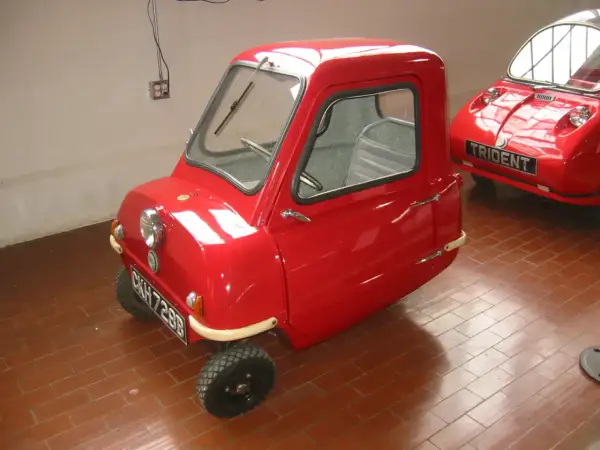 Czerwony, trójkołowy samochód Peel P50, najmniejszy pojazd na świecie, stoi na ceglanej podłodze.