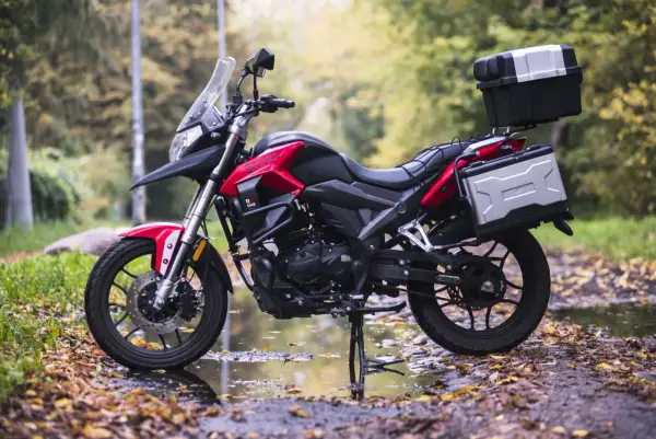 Czerwony motocykl turystyczny z kuframi, zaparkowany na jesiennej drodze. Model kat a1 gotowy na przygodę.
