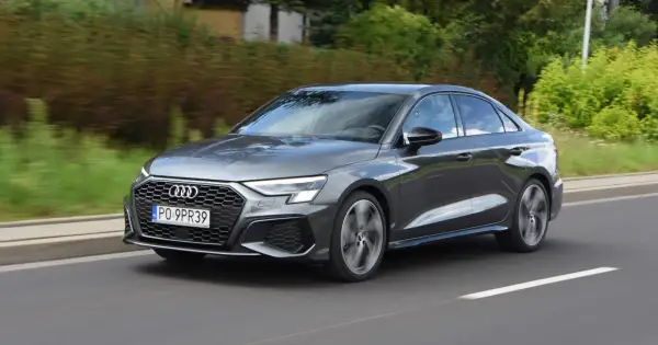 Szary Audi a3 sedan jedzie po drodze, otoczony zielenią.