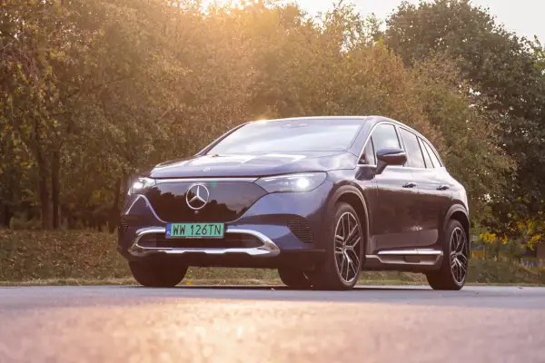 Elegancki, ciemnogranatowy Mercedes EQE SUV lśni w jesiennym słońcu na tle drzew.