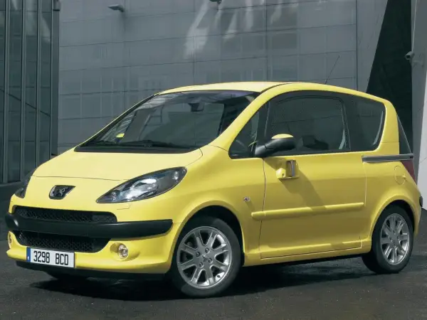 Żółty Peugeot 1007 z przesuwnymi drzwiami na tle nowoczesnego budynku.