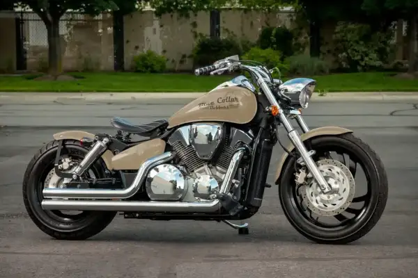 Beżowy motocykl Honda VTX 1300 z chromowanymi elementami i napisem "Blue Collar Bobbers" na baku, zaparkowany na ulicy.